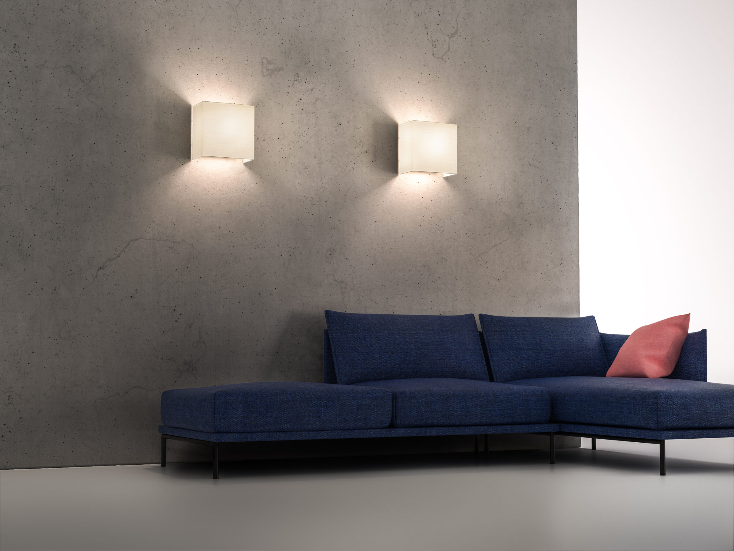 Two CUBIC BOX wall lamps in white on concrete wall above blue sofa.