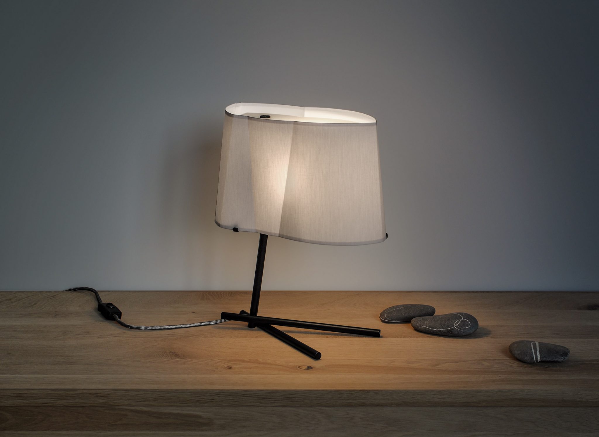 Bent Bird table lamp on a sideboard decorated with stones.