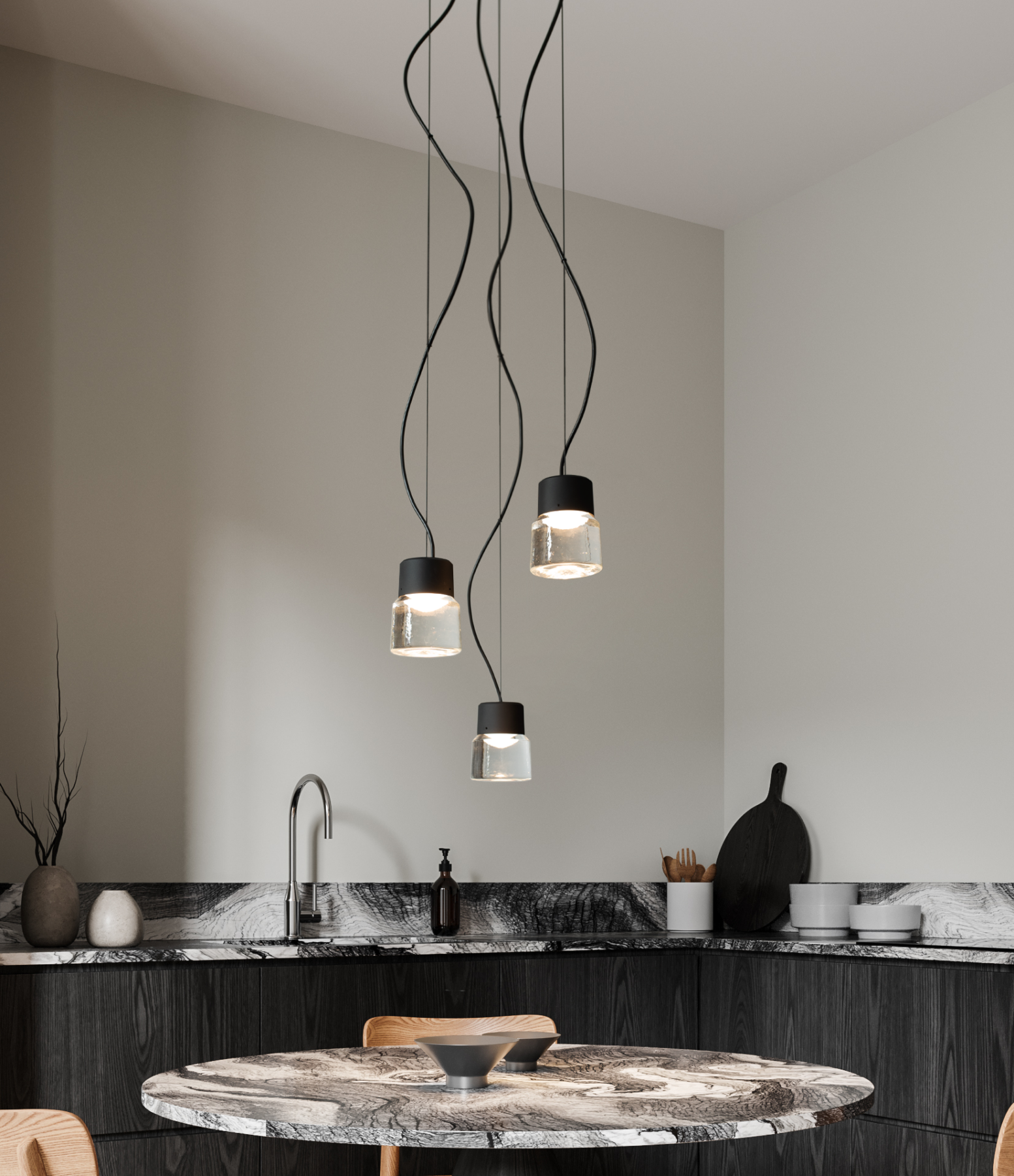 The CAST P pendant light is suspended as a set of three above a stylish round marble table. In the background, a stylish kitchen in black-stained wood and marble.