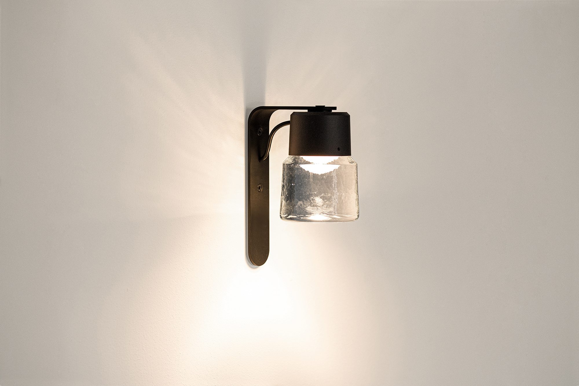 Cast LED wall lamp made of cast glass and black anodised aluminium.
