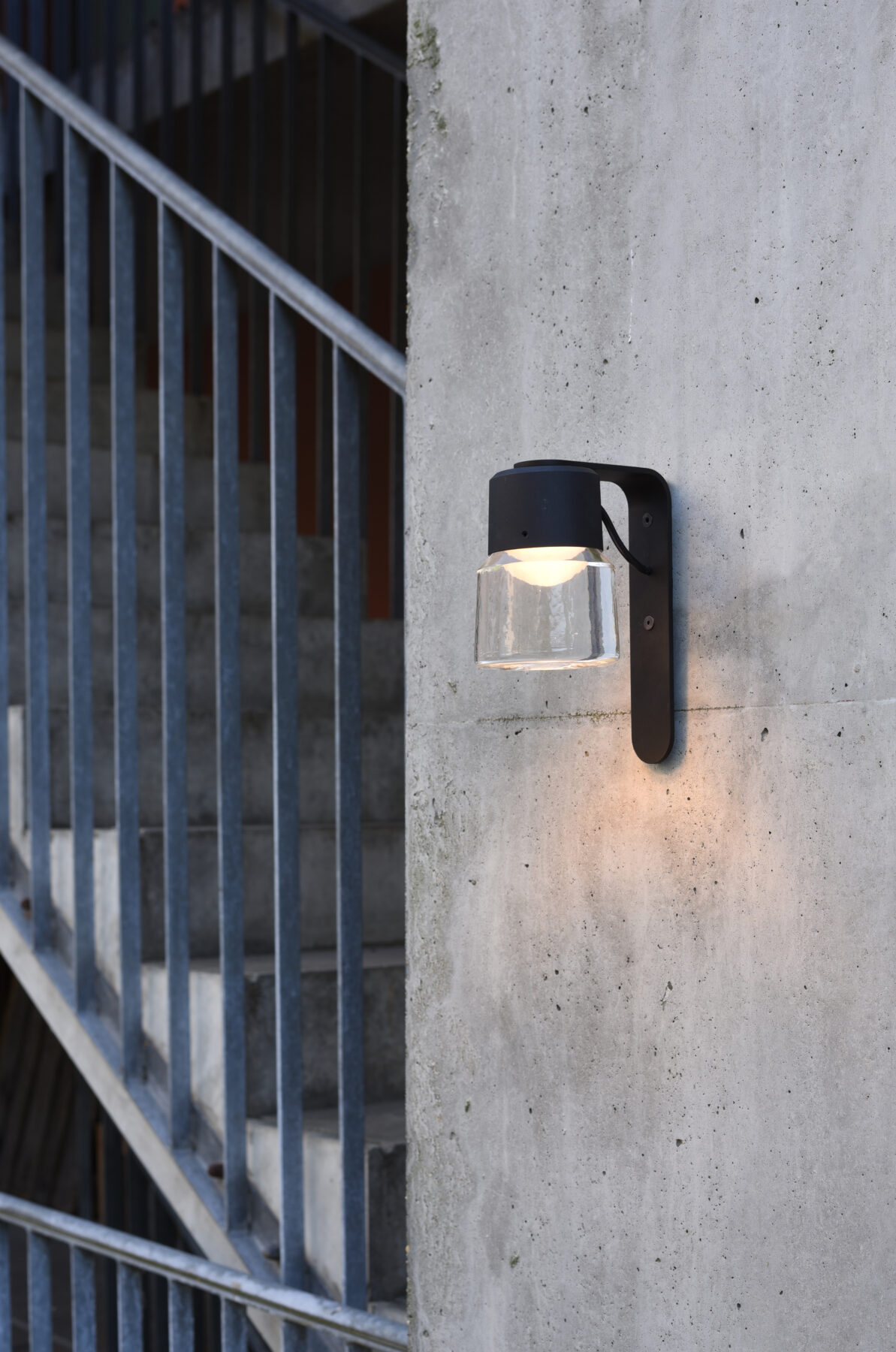 The CAST W cast glass luminaire with black aluminum body and wall bracket as exterior lighting for a modern staircase gallery.
