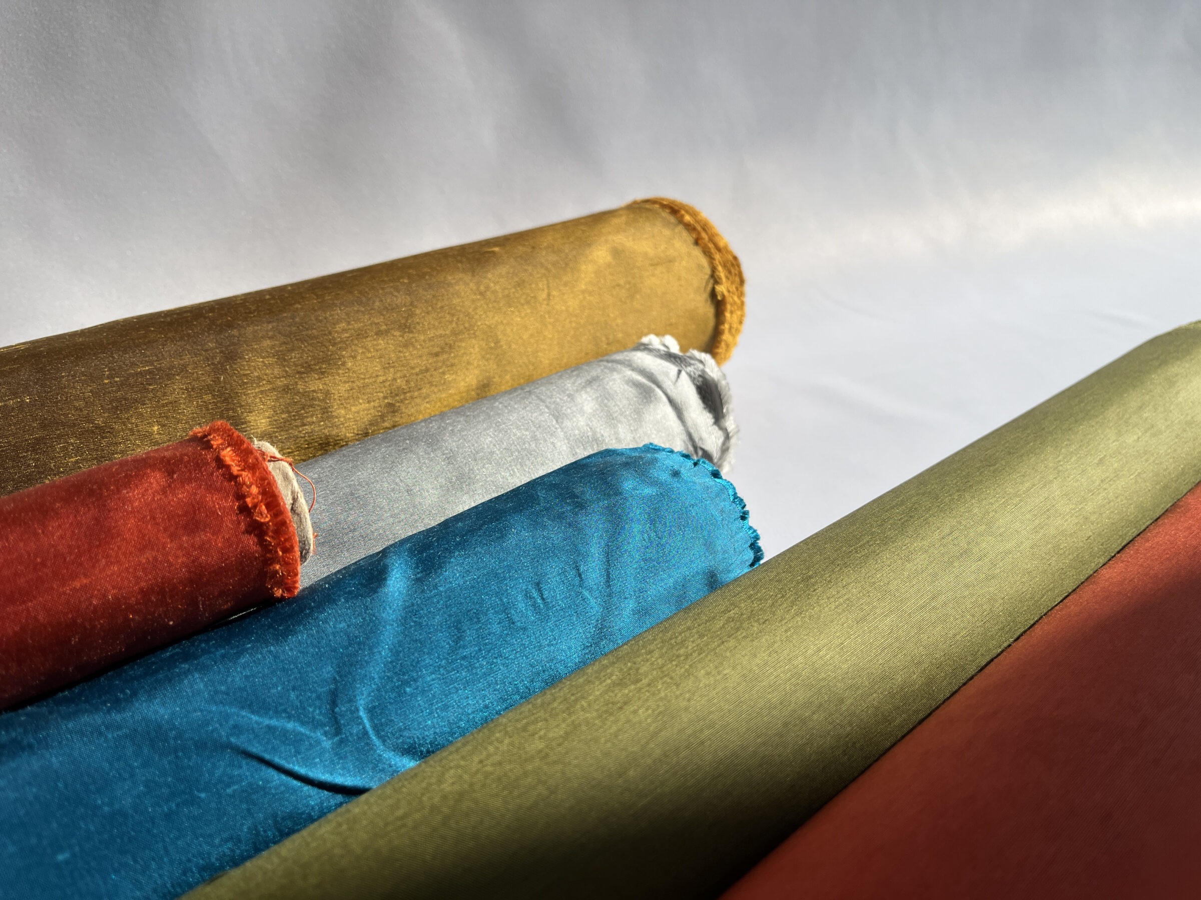 Dupioni silks and chintz fabrics for fabric shade lamps rolled up in various rich colours.